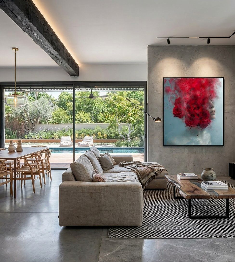 Open living space in a Hod Hasharon villa, a large figurative artwork of a woman's face dissolving into red roses on a concrete wall, garden and pool beyond the glass