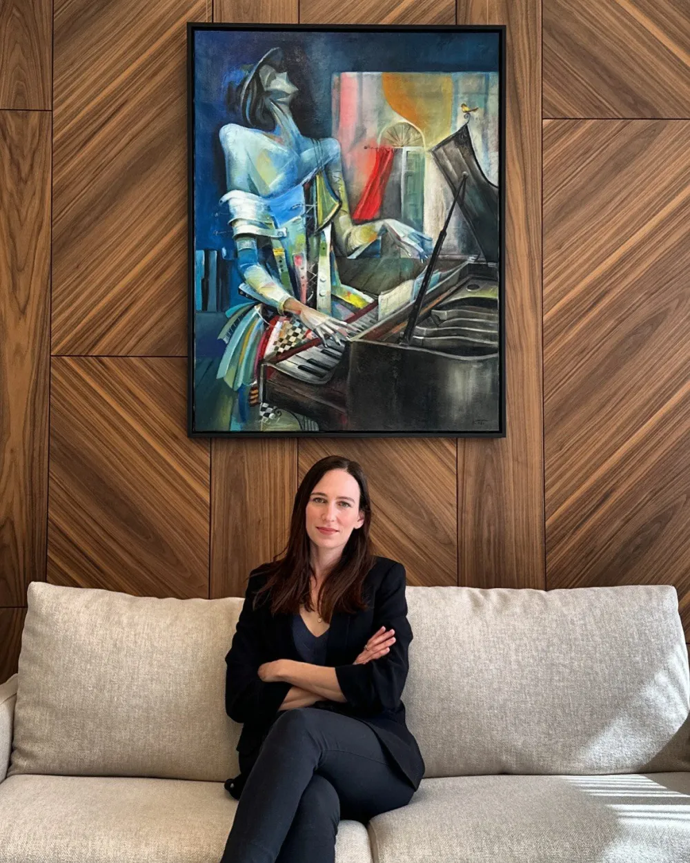 Stav Theodor seated on a pale linen sofa beneath a framed painting of a woman playing the piano, hung on a walnut panelled wall